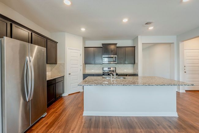 Kitchen with dark brown cabinets, light stone countertops, stainless steel appliances, dark wood-type flooring, and visible vents | Image 5