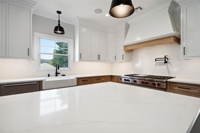 Kitchen featuring wall chimney exhaust hood, decorative backsplash, pendant lighting, white cabinets, and ornamental molding | Image 10