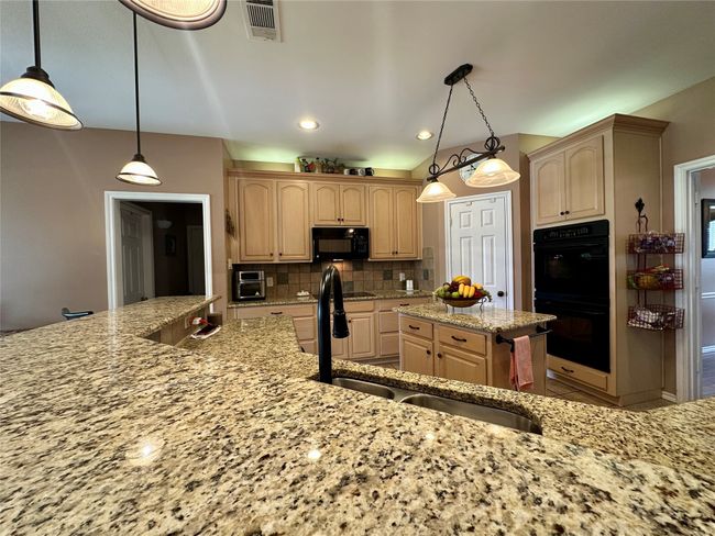 Kitchen with tasteful backsplash, a sink, light stone counters, visible vents, and black appliances | Image 9
