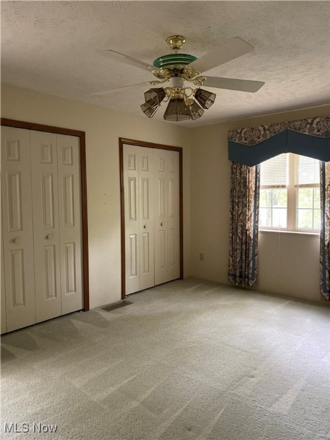 Unfurnished bedroom featuring light carpet, two closets, a textured ceiling, and ceiling fan | Image 12