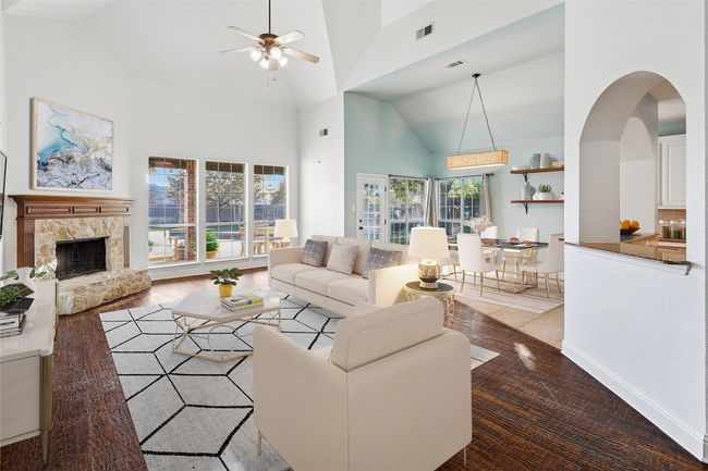 Living area with a fireplace with raised hearth, high vaulted ceiling, visible vents, and a ceiling fan | Image 5