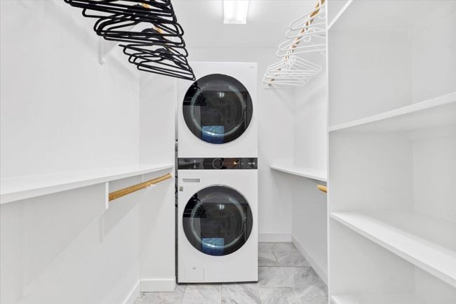 Laundry room featuring estacked washer and dryer and light marble finish flooring | Image 17