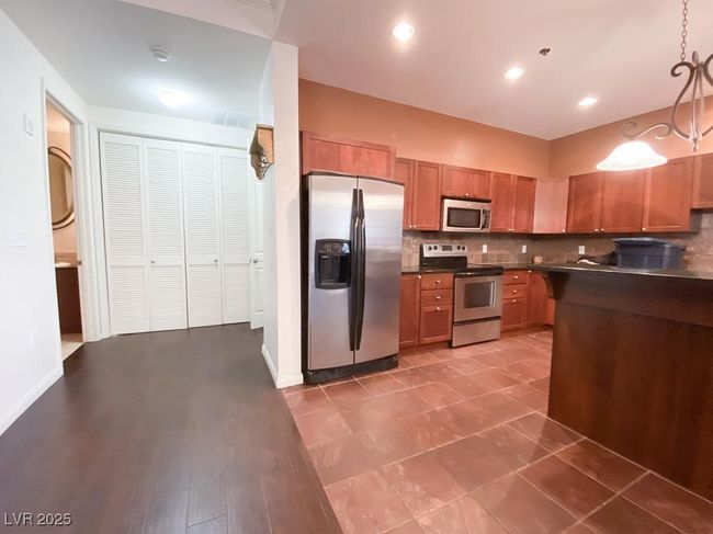 Kitchen featuring appliances with stainless steel finishes, dark countertops, tasteful backsplash, brown cabinets, and pendant lighting | Image 5