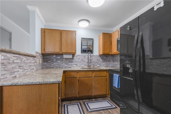 Kitchen featuring black appliances, brown cabinets, tasteful backsplash, crown molding, and light stone countertops | Image 5