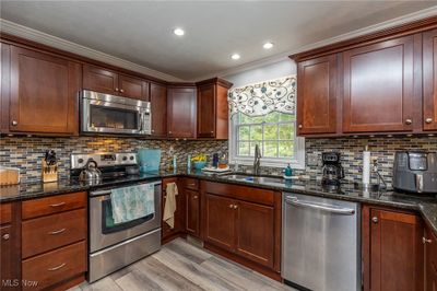 Kitchen featuring dark stone counters, light hardwood / wood-style floors, sink, stainless steel appliances, and crown molding | Image 2