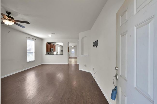 This photo showcases an open-concept living area and or living/dining combo with hardwood floors and neutral walls. The room features a ceiling fan, large windows for natural light, and a view into the kitchen with modern cabinetry. Perfect for family gatherings and entertaining. | Image 4
