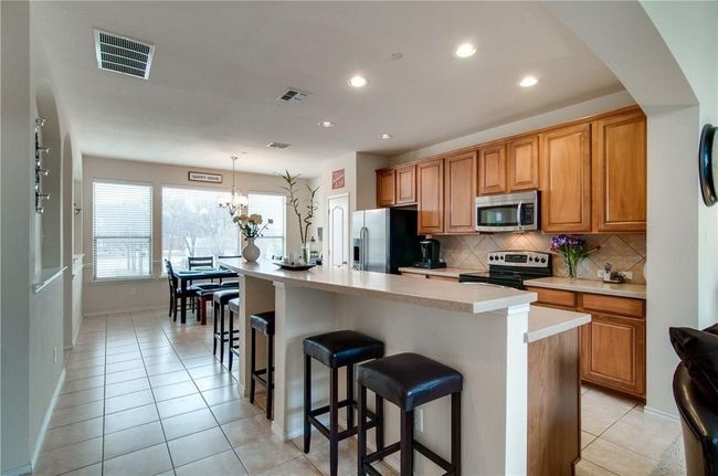 Kitchen featuring pendant lighting, appliances with stainless steel finishes, a kitchen breakfast bar, and a center island with sink | Image 4