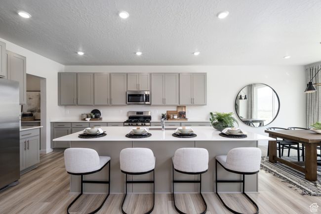 Kitchen featuring stainless steel appliances, gray cabinetry, a breakfast bar, light countertops, and light wood-style flooring | Image 5
