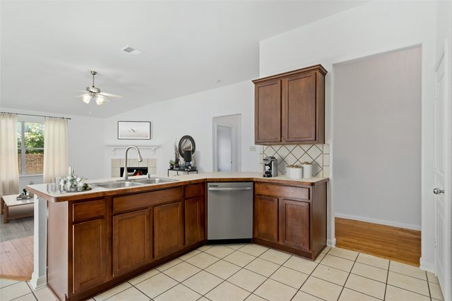 Kitchen featuring stainless steel dishwasher, light countertops, decorative backsplash, a ceiling fan, and a peninsula | Image 12