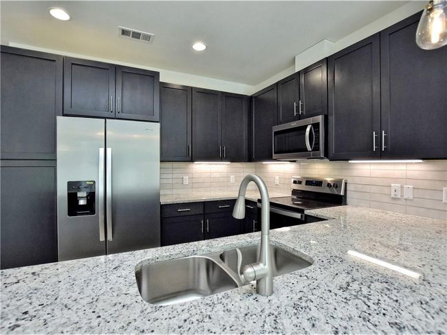 Kitchen featuring appliances with stainless steel finishes, tasteful backsplash, light stone counters, dark cabinetry, and recessed lighting | Image 11