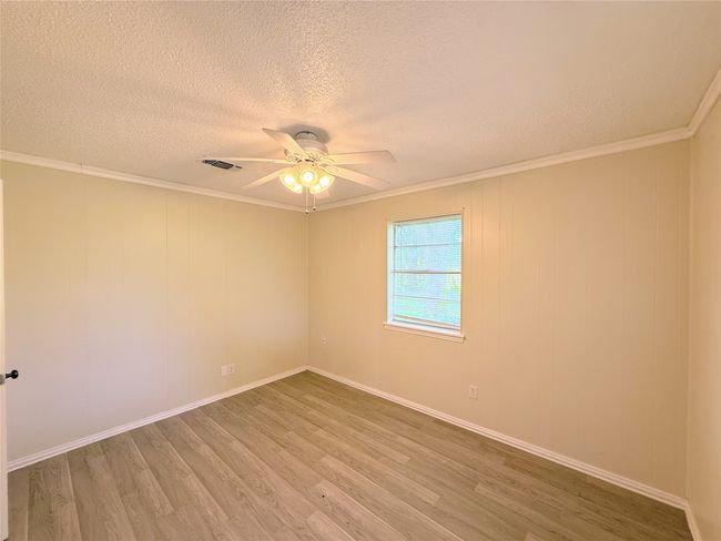 Empty room with light wood-style floors, ceiling fan, a textured ceiling, and crown molding | Image 15
