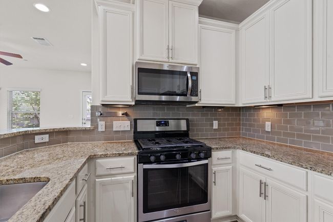Kitchen featuring appliances with stainless steel finishes, white cabinetry, ceiling fan, decorative backsplash, and light stone countertops | Image 13