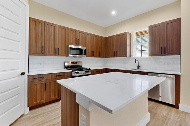 Kitchen with stainless steel appliances, light wood-style flooring, tasteful backsplash, a center island, and light stone counters | Image 12