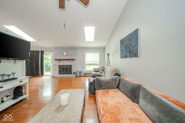 living area with a skylight, light wood-style flooring, vaulted ceiling, a brick fireplace, and a ceiling fan | Image 9
