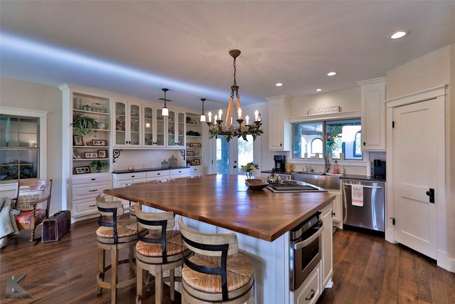 Kitchen featuring appliances with stainless steel finishes, butcher block countertops, a chandelier, white cabinetry, and a kitchen bar | Image 10