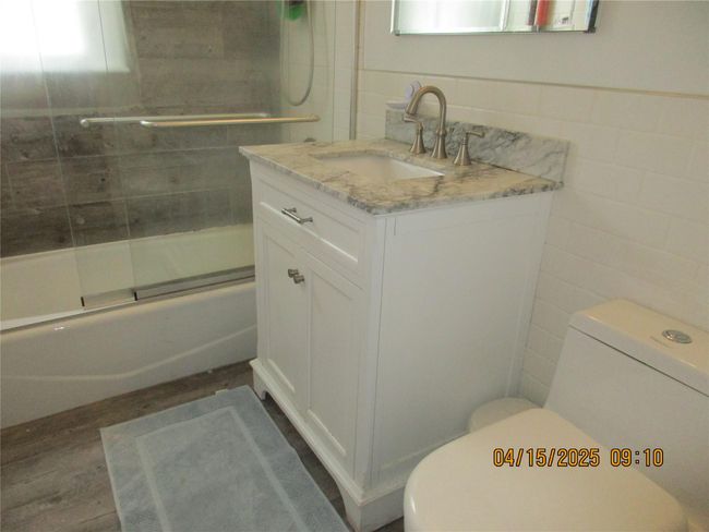 Full bath featuring toilet, tile walls, vanity, wood finished floors, and shower / bath combination with glass door | Image 13