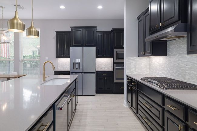 Kitchen featuring appliances with stainless steel finishes, a sink, under cabinet range hood, light countertops, and hanging light fixtures | Image 9