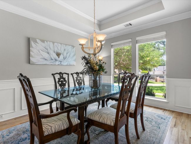 Dining room featuring a raised ceiling, a chandelier, healthy amount of natural light, wainscoting, and light wood-type flooring | Image 7