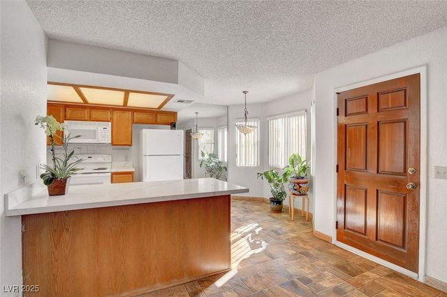 Kitchen with baseboards, white appliances, a peninsula, light countertops, and hanging light fixtures | Image 7