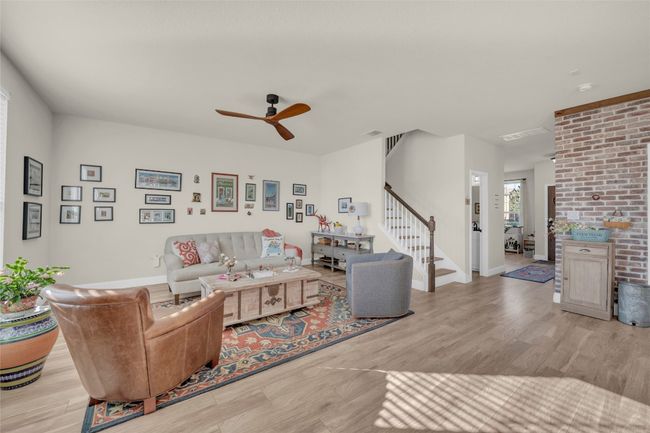 Living room with baseboards, visible vents, brick wall, light wood-style flooring, and stairs open to the dining and kitchen | Image 9
