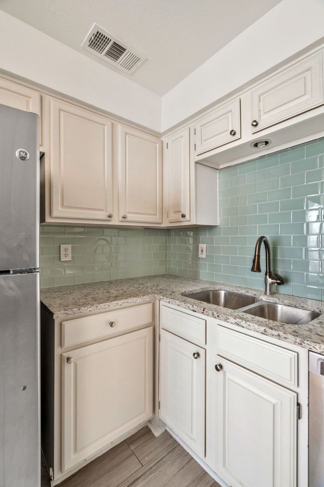 Kitchen with a sink, decorative backsplash, dishwasher, visible vents, and freestanding refrigerator | Image 10