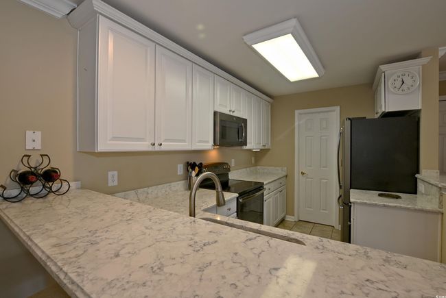 Kitchen featuring white cabinets, light tile patterned floors, light stone counters, kitchen peninsula, and stainless steel appliances | Image 7