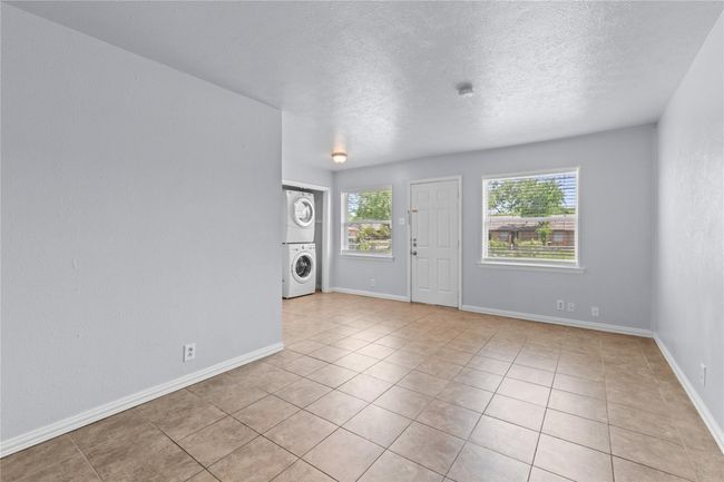 Empty room with stacked washing machine and dryer, light tile patterned floors, and a textured ceiling | Image 7