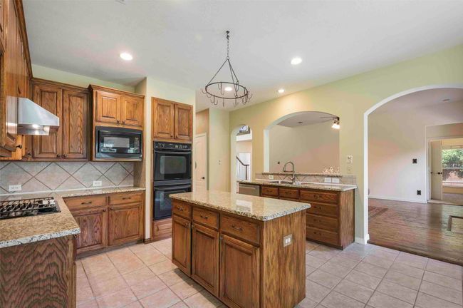 Kitchen featuring arched walkways, light tile patterned floors, wall chimney range hood, black appliances, and a sink | Image 13