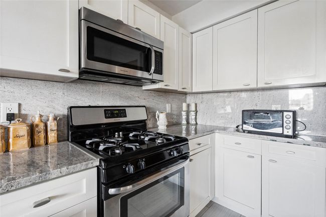 Kitchen featuring stainless steel appliances, light stone countertops, white cabinetry, and decorative backsplash | Image 11