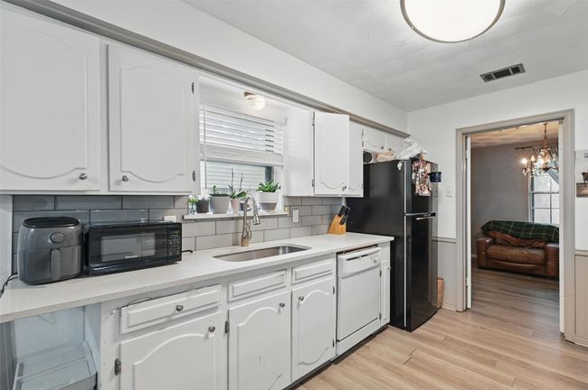 Kitchen with black appliances, a sink, tasteful backsplash, white cabinetry, and a chandelier | Image 6