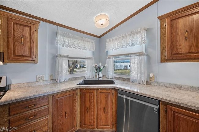 Kitchen with dishwasher, brown cabinets, ornamental molding, a textured ceiling, and lofted ceiling | Image 7