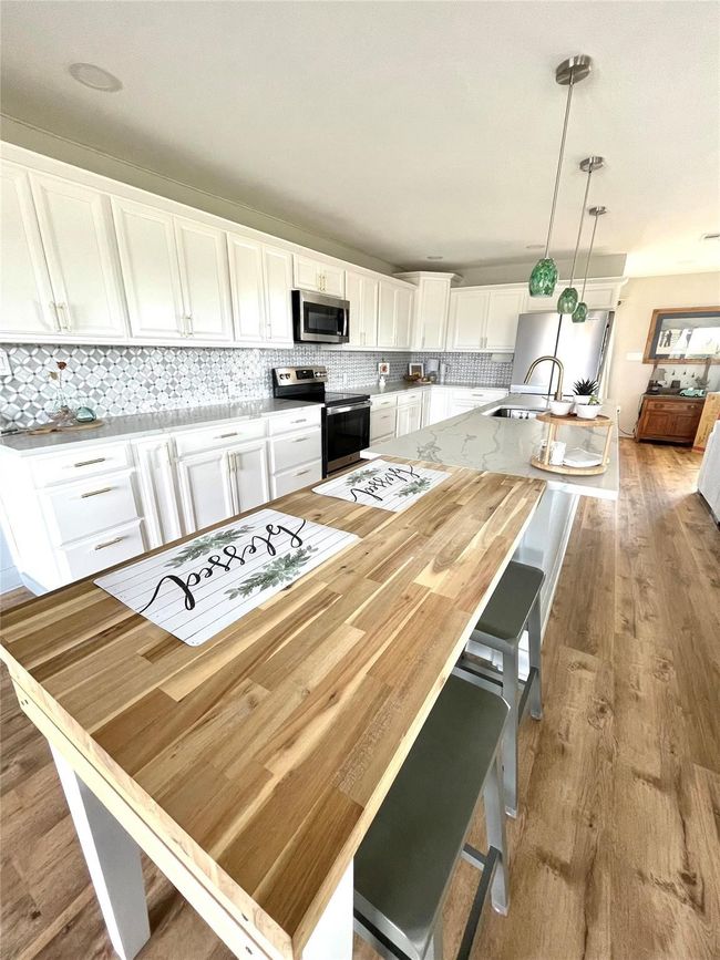 Kitchen featuring appliances with stainless steel finishes, light wood-style flooring, white cabinets, tasteful backsplash, and a large island with sink | Image 5