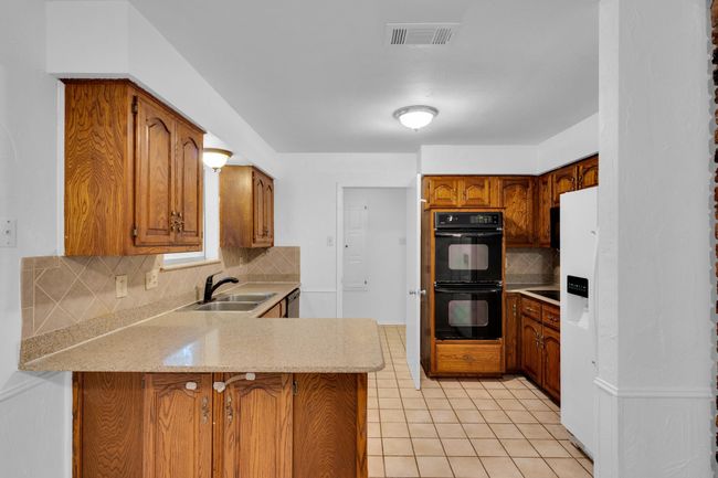 Kitchen with dobule oven black, visible vents, a peninsula, tasteful backsplash, and a sink | Image 14