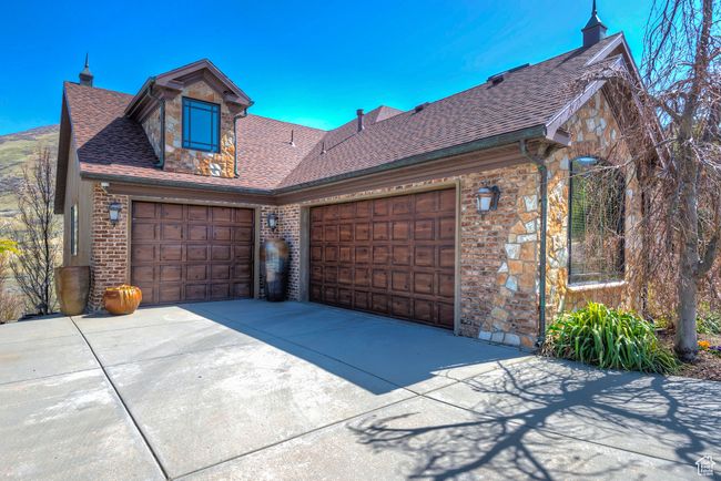 View of front of property featuring an attached garage, driveway, a shingled roof, and stone siding | Image 66