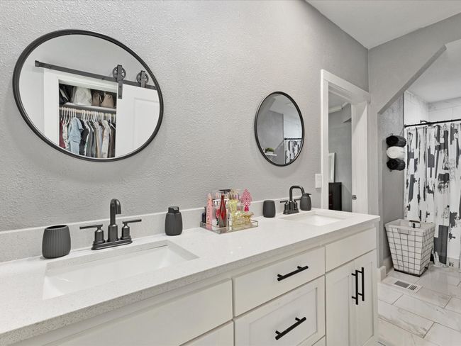 Bathroom with double vanity, a shower with curtain, a textured wall, a spacious closet, and marble look tile flooring | Image 13