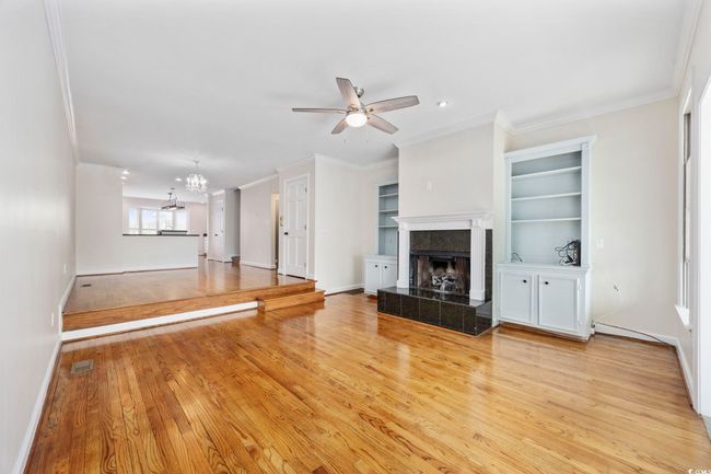 Unfurnished living room featuring a tiled fireplace, ornamental molding, ceiling fan, a chandelier, and baseboards | Image 11