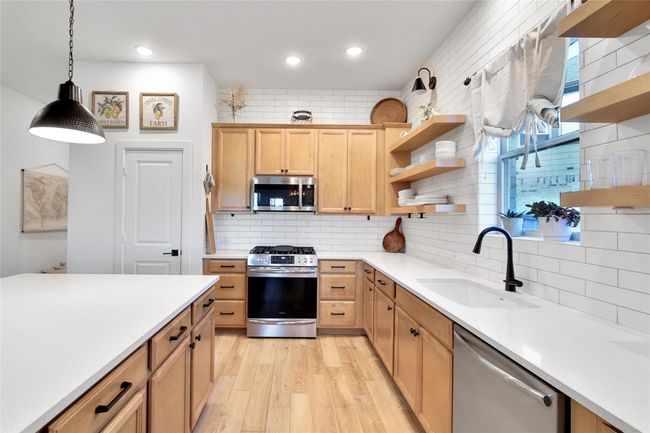 This kitchen features modern design with light wood cabinetry, white subway tile backsplash, and open shelving. It includes stainless steel appliances, a large island with pendant lighting, and a window above the sink, creating a bright and welcoming space. | Image 21