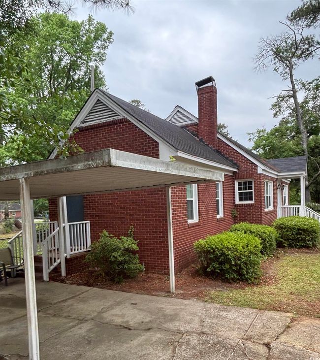 View of property exterior featuring brick siding, a chimney, and a carport | Image 4