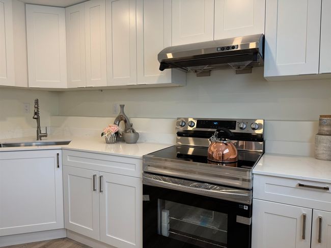 Kitchen with stainless steel electric stove, range hood, and white cabinets | Image 24
