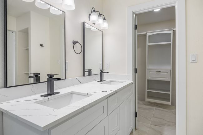 Bathroom with a walk in closet, double vanity, light marble finish floors, and a chandelier | Image 30