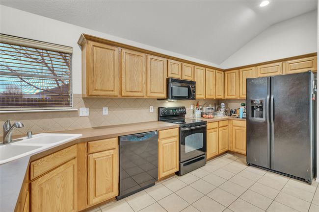 Kitchen featuring black appliances, vaulted ceiling, decorative backsplash, light countertops, and light tile patterned floors | Image 16