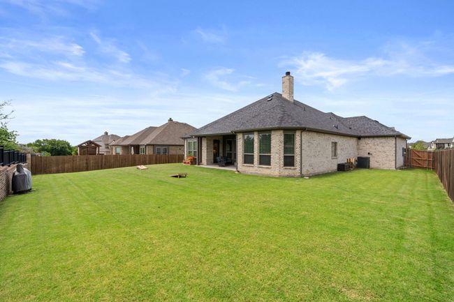 Rear view of property with a fenced backyard, brick siding, a chimney, a patio, and a shingled roof | Image 37