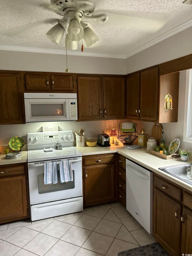 Kitchen with white appliances, a textured ceiling, light countertops, ornamental molding, and light tile patterned flooring | Image 6