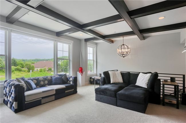 This sophisticated family room features a coffered ceiling, built-in lighted cabinetry, and a dramatic fireplace with marble surround—framed by oversized windows that flood the space with natural light and lush views, all seamlessly connected to the designer kitchen. | Image 23