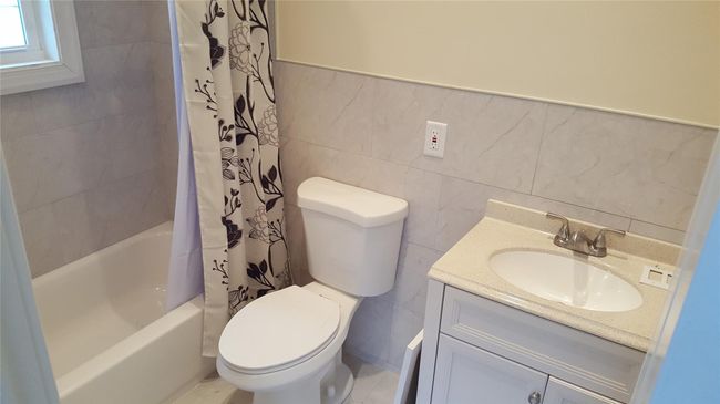 Full bathroom with tile walls, toilet, shower / bath combo, and vanity | Image 9