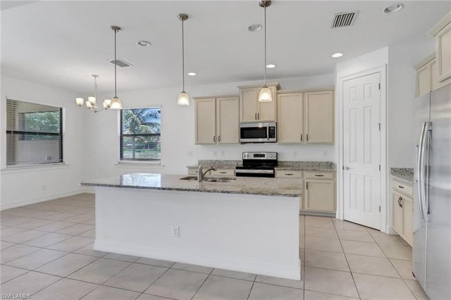 Kitchen with appliances with stainless steel finishes, a sink, light stone countertops, a chandelier, and light tile patterned floors | Image 26