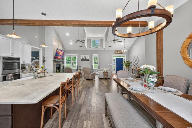 Dining space featuring ceiling fan, beamed ceiling, dark wood-type flooring, a fireplace, and high vaulted ceiling | Image 15