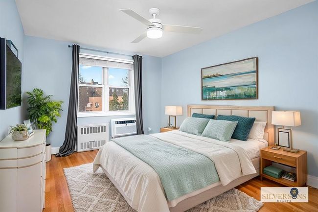 Bedroom featuring radiator heating unit, light wood-type flooring, a wall unit AC, and ceiling fan | Image 14