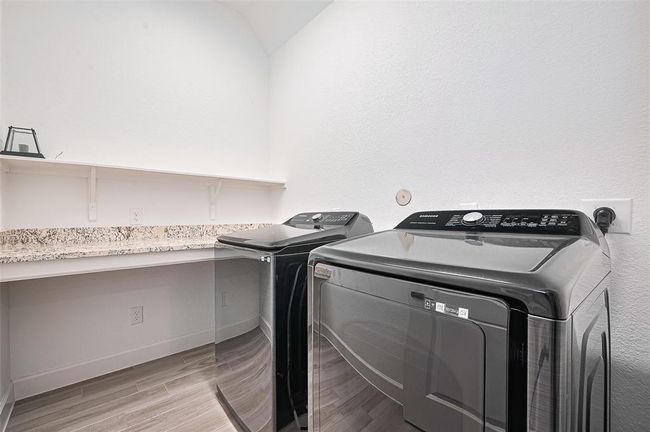 This well-appointed utility room features a modern washer and dryer setup, granite countertop workspace, and upper shelving for convenient storage | Image 15