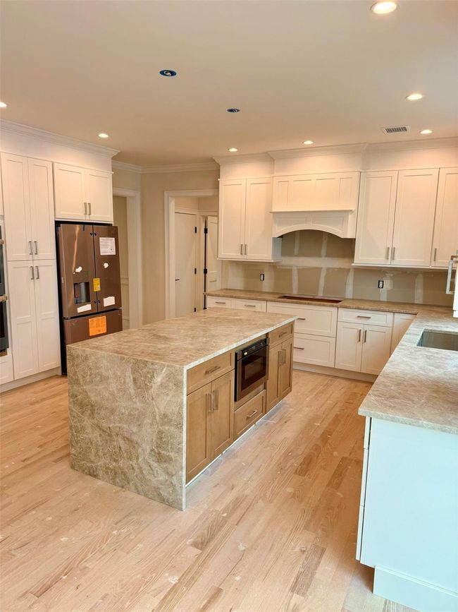 Kitchen with stainless steel fridge with ice dispenser, recessed lighting, light stone countertops, light wood-style flooring, and ornamental molding | Image 5